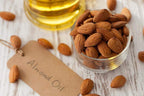 Glass container of almonds with a jar of almond oil on a wooden surface.